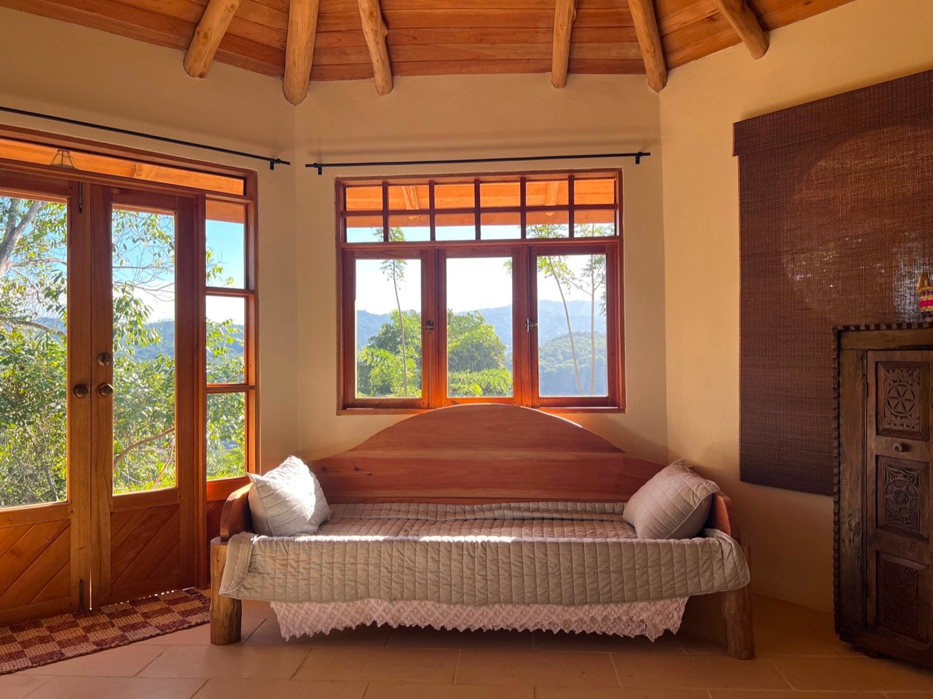 Timber daybed beside windows overlooking the hills of Puriscal