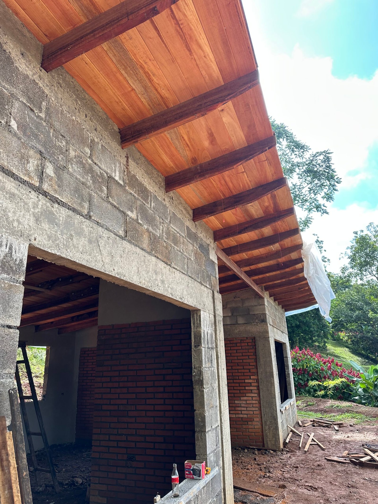 Cedar ceiling boards and dark pilón rafters above unfinished block and brick walls at Alon’s house in Puriscal.